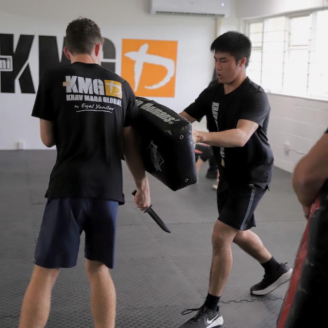 Krav Maga Auckland student using a focus shield to defend a rubber-knife attack — training the principle of using a shield-like object such as a chair or bag in real situations