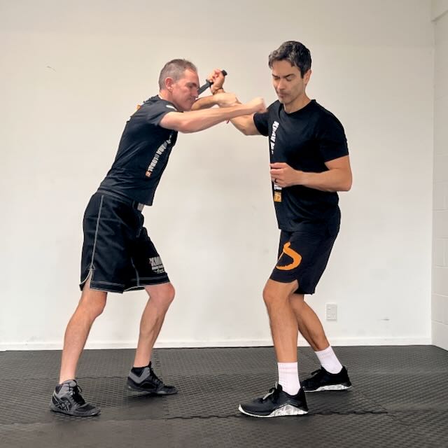 KMG New Zealand students practising a defence against an overhand knife attack — weapons scenarios are integrated from beginner level