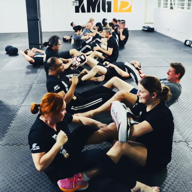 KMG New Zealand students doing situps as part of a training drill — combining fitness conditioning with striking technique