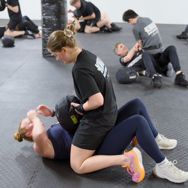 Krav Maga Auckland students doing a partner conditioning drill, one doing sit-ups while the other holds a weighted bag