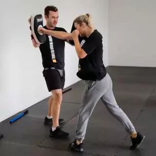 Woman throwing a straight punch into a focus pad held by an instructor at Krav Maga Auckland
