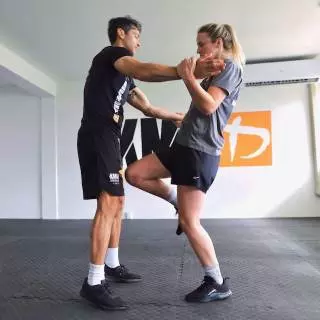 Woman practising a choke release with a knee strike against an instructor at Krav Maga Auckland
