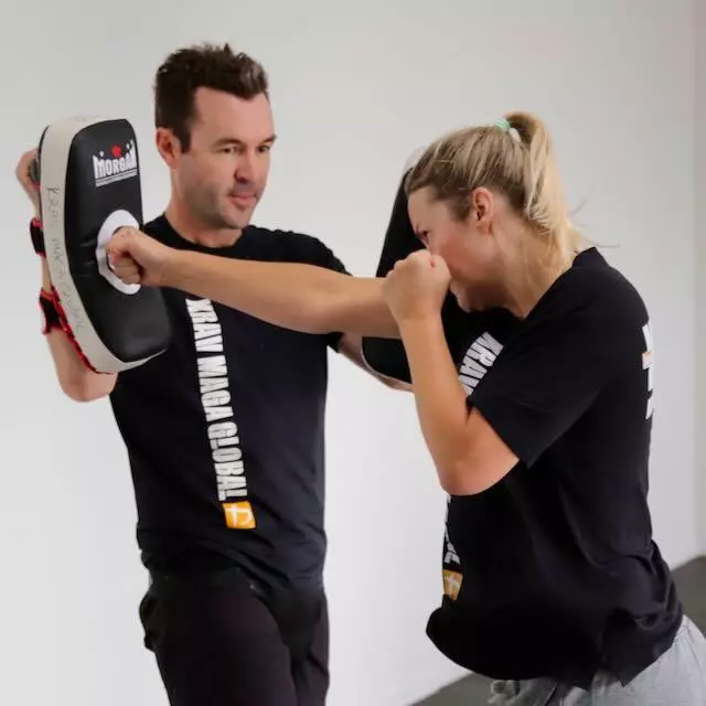 Instructor holding focus pads and coaching a member's punch at Krav Maga Auckland