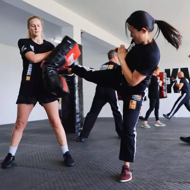 Woman performing a controlled round kick to pads during a women's self-defence class at Krav Maga Auckland