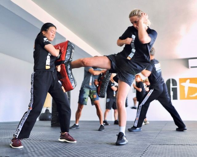 Woman delivering a roundhouse kick to focus pads during a Krav Maga self defence class in Birkenhead Auckland.